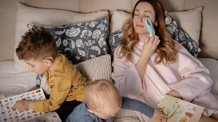 Mother's day a mom enjoying time with young children playing on the bed as she does skincare